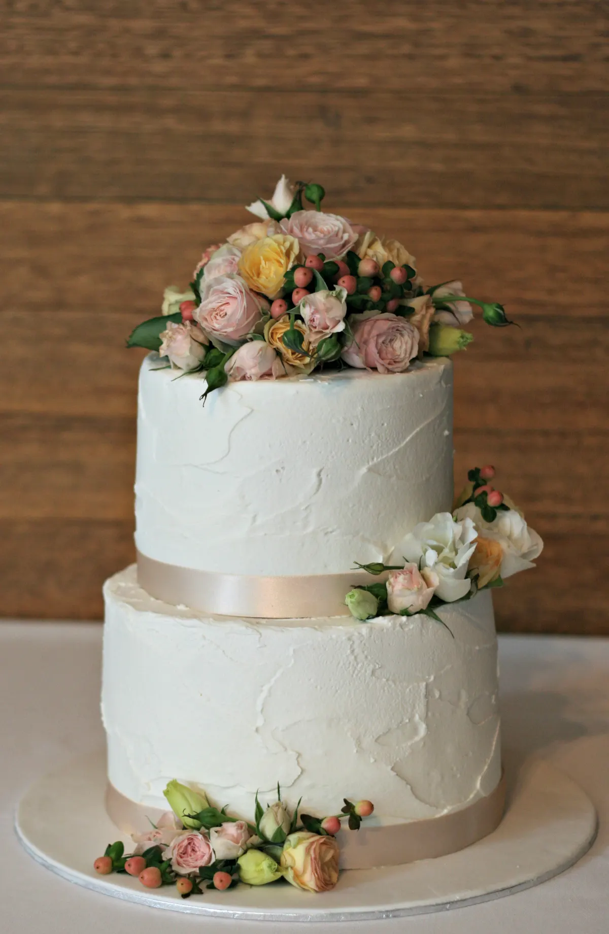 A two-tier white buttercream wedding cake topped and trimmed with pink and peach roses