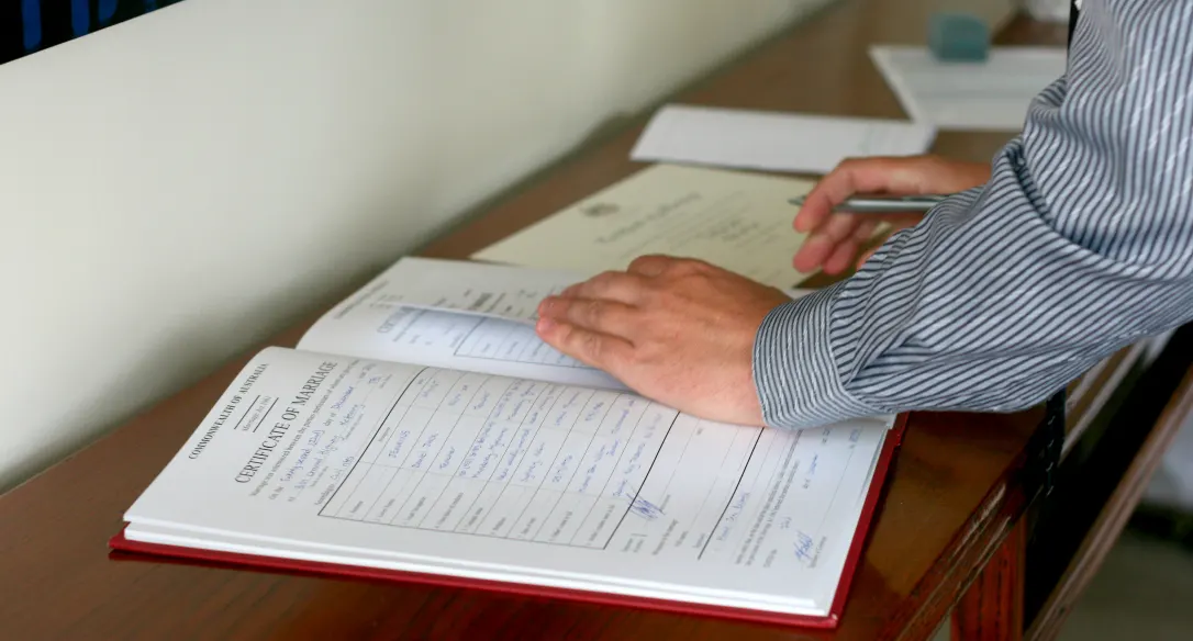 A hand resting on the open marriage register beside a pen and certificate